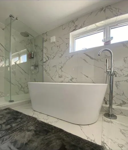 Freestanding bath with floor-mounted tap in a marble-effect tiled bathroom