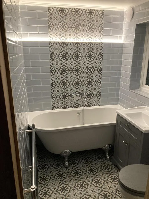 Finished bathroom with roll-top bath, patterned floor tiles and feature tile panel