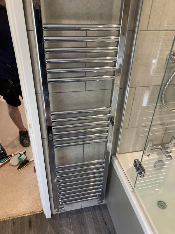 Tall chrome heated towel rail beside a glass bath screen